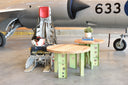 "Floor beam accent table with ash wood top and green aluminum aircraft beam legs, staged by a CF104 aircraft and ejection seat