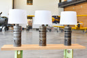 Collection of table lamps made from Combustion liners from an aircraft engine. Various shades of burnishing from engine heat. White linen shade