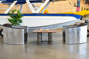 Square coffee table with a clear stained walnut wood top. Legs are 4 combustion liners from an aircraft engine. Staged in front of a turbo beaver aircraft with chairs
